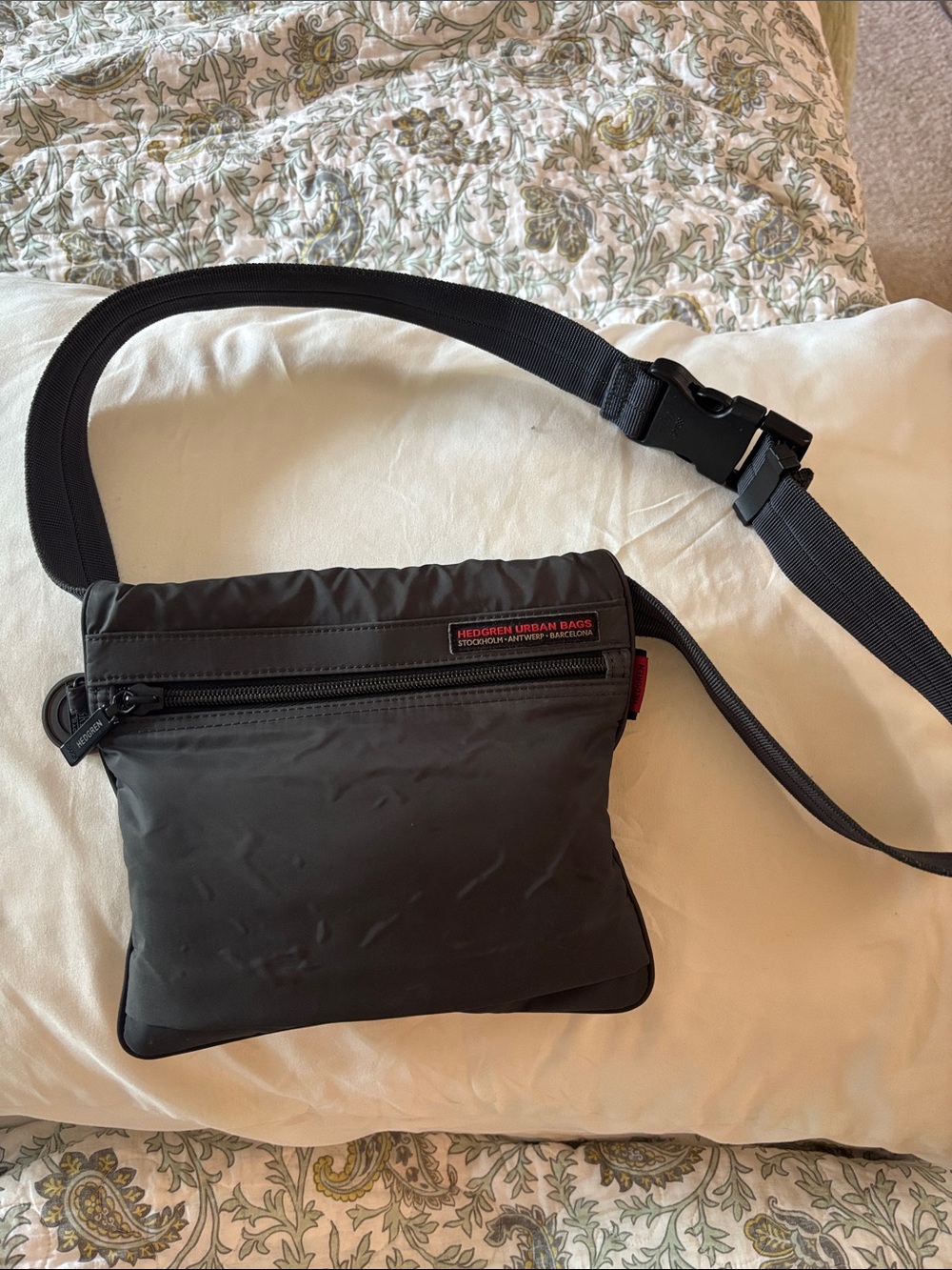 This grey Hedgren crossbody bag features a distinctive red label showcasing the